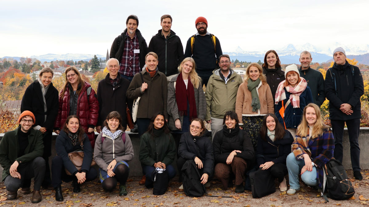 Group of about 20 people in autumn, outdoors, mountains in the background, all dressed warmly.