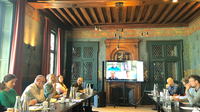 Participants in a wood-panelled room and other participants via video conference