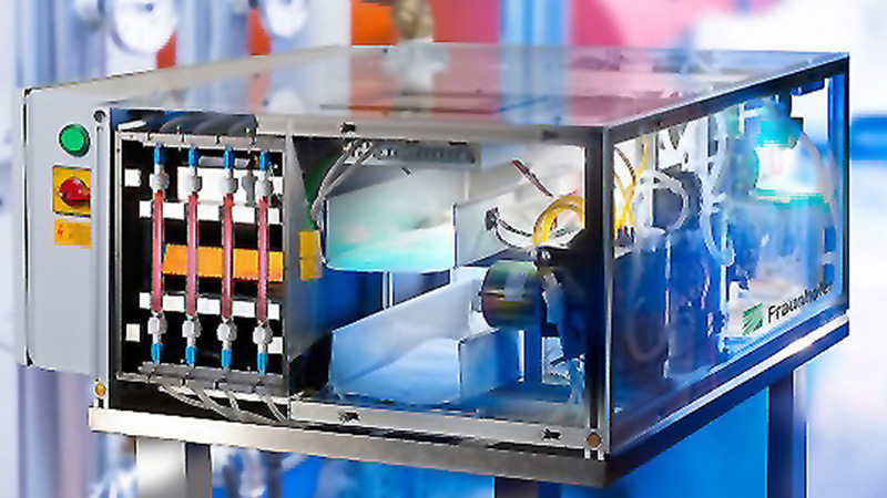 Abgebildet ist der Prototy des biologischen Breitbandsensors AquaBioTox. Sichtbar ist ein gläserne Kiste, die verschiedene Apparaturen für den Wassertransport, Messystem und Elektronik enthält