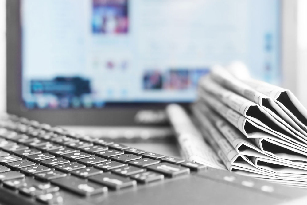 Tastatur und Zeitungsstapel vor Bildschirm mit Newsseite